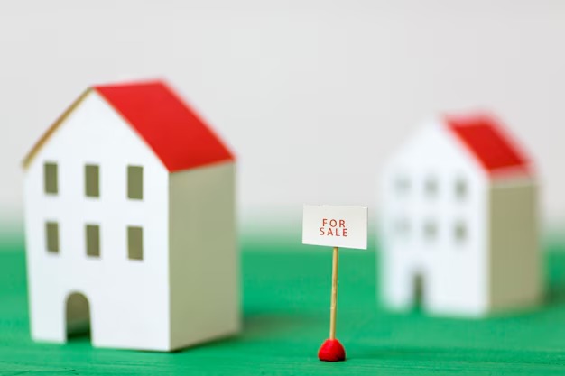 Small paper houses with a red stick and a "For Sale" sign displayed prominently in front of them