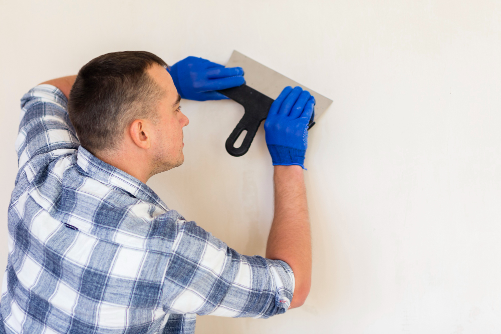 Man in a checked shirt and blue gloves smoothing a wall with a trowel